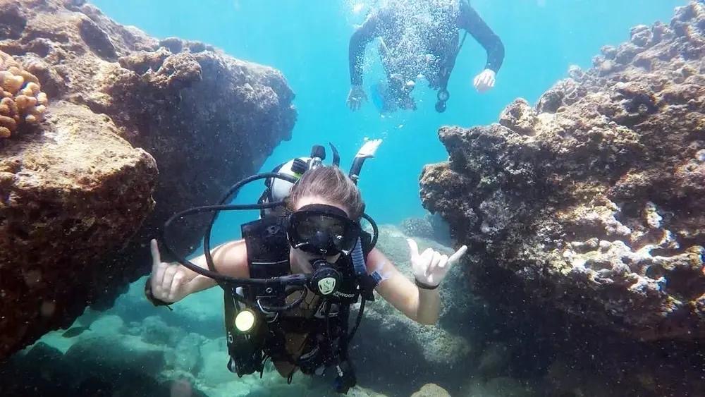 Scuba divers giving a shaka among rock formations underwater in San Juan